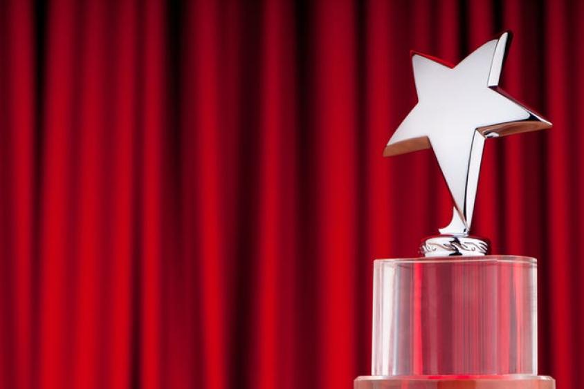 Image of clear trophy with a silver star topper in front of red theatre curtains